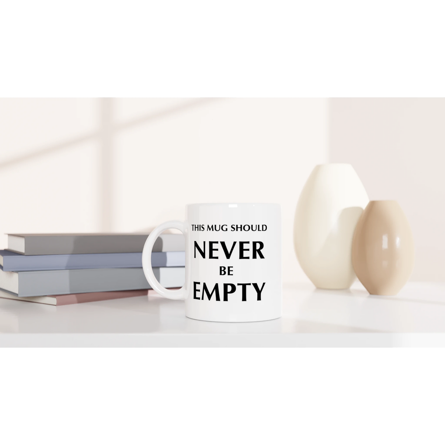Astral Apple white, microwave and dishwasher safe, 11oz, ceramic mug with graphic print of the text, “This Mug Should Never Be Empty”, on a desk, funny mug design