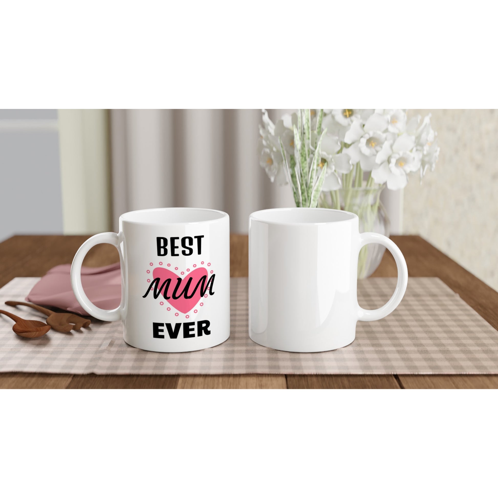 Front and back view of two white ceramic mug with the words "Best Mum Ever" in black and a picture of a pink heart on a table.