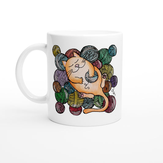 White ceramic mug with a watercolour painting of a ginger cat sleeping happily amongst balls of coloured yarn