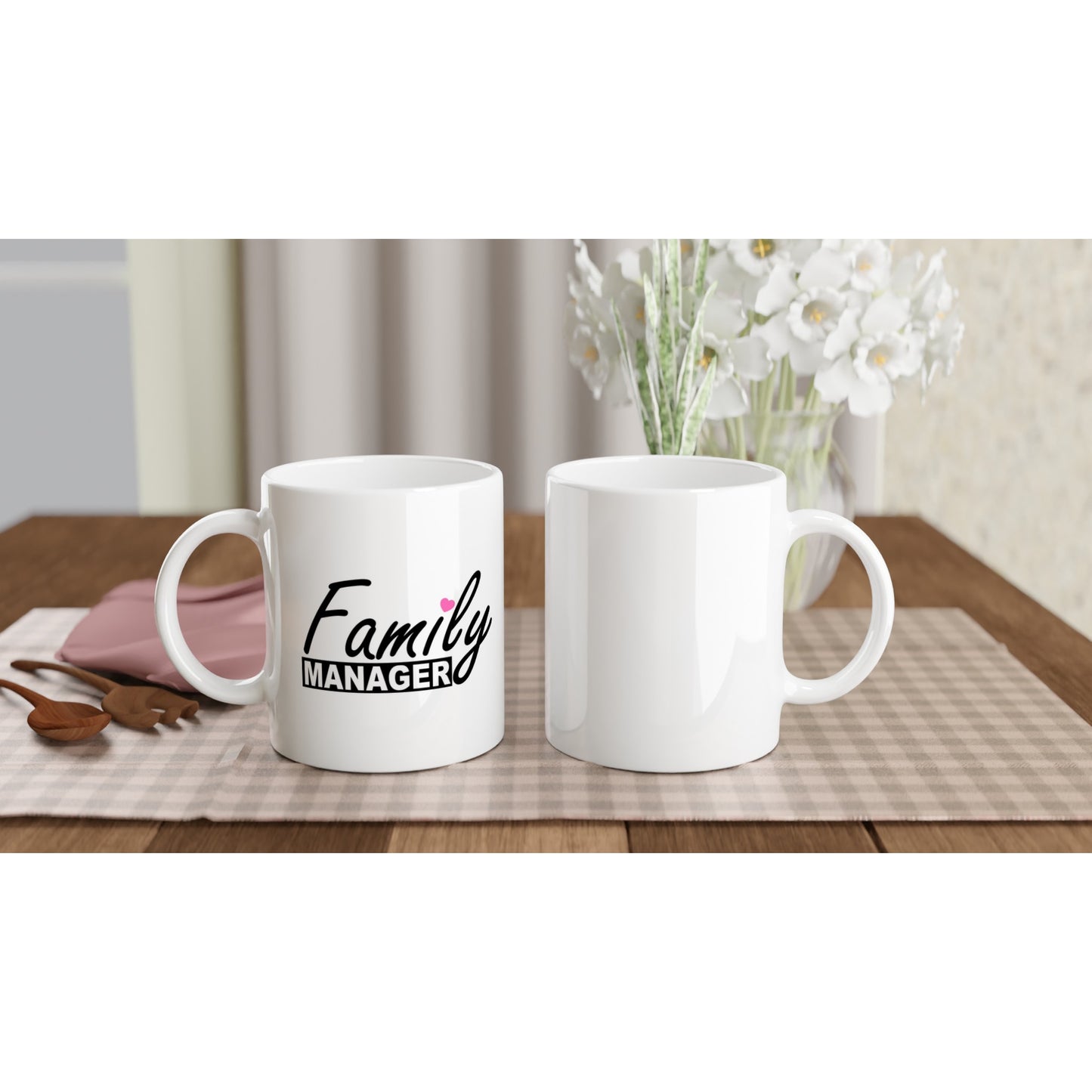 Front and back view of white ceramic mug with the words "family manager" in black, where the letter "i" in family is dotted with a small pink heart.