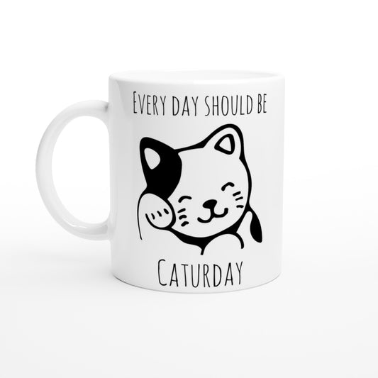 White ceramic mug with the pun, "Every day should be Caturday" and an image of a grooming cat on it in black.