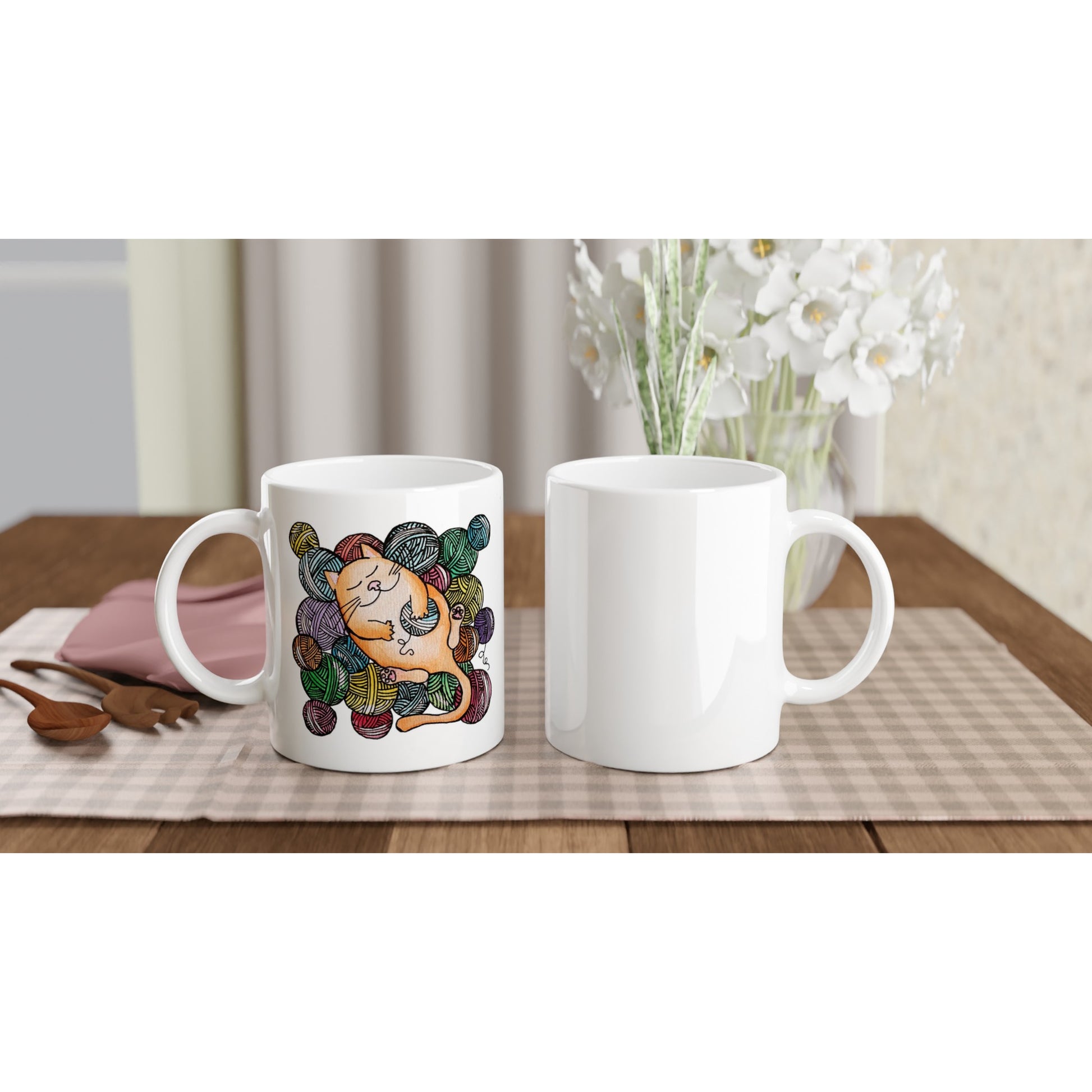 The front and back view of a white ceramic mug with a watercolour painting of a ginger cat sleeping happily amongst balls of coloured yarn