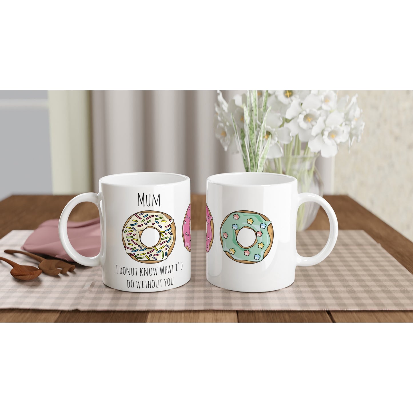 The front and back view of a white ceramic mug with the words, "Mum, I donut know what I'd do without you" in black and illustrations of donuts with white icing and multicoloured rainbow sprinkles, a pink iced donut with white sprinkles and a pastel green iced donut with flower shaped sprinkles