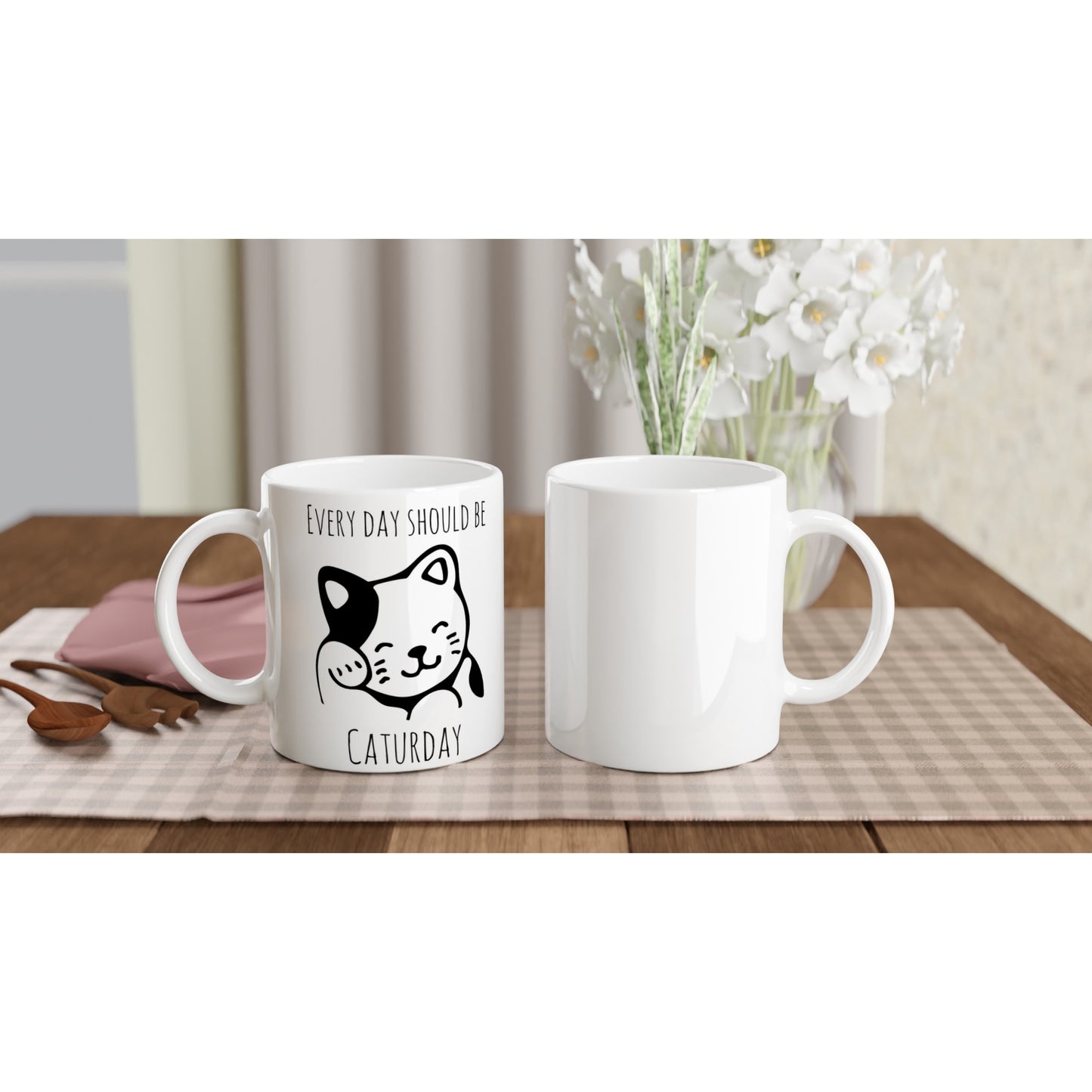 White ceramic mug, front and back views, with the pun, "Every day should be Caturday" and an image of a grooming cat on it in black.