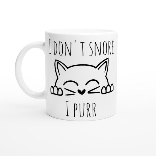 A white ceramic mug with the words "I don't snore, I purr" and an image of a cat peeping up happily, in black