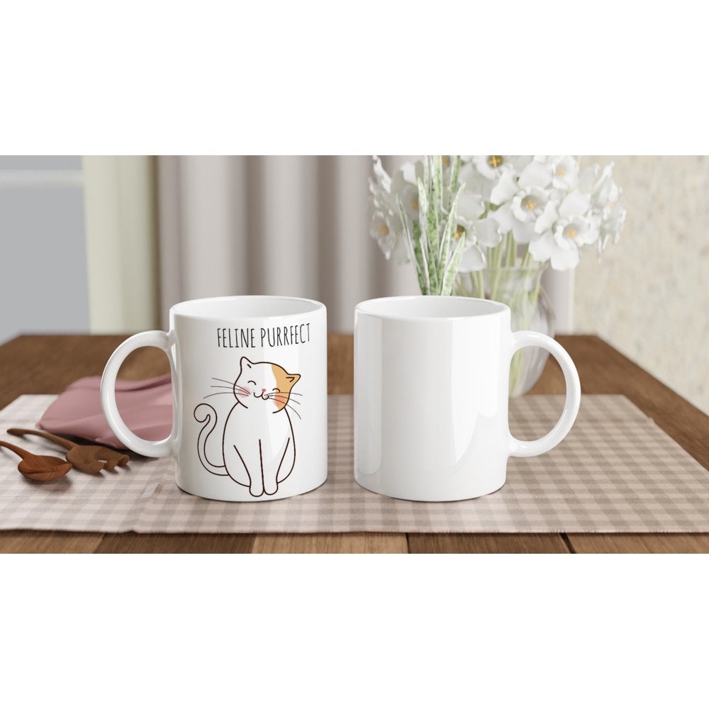 2 white ceramic mugs, front and back view, with the words "Feline purrfect" in black and a picture of a white and light brown cat smiling and sitting happily.