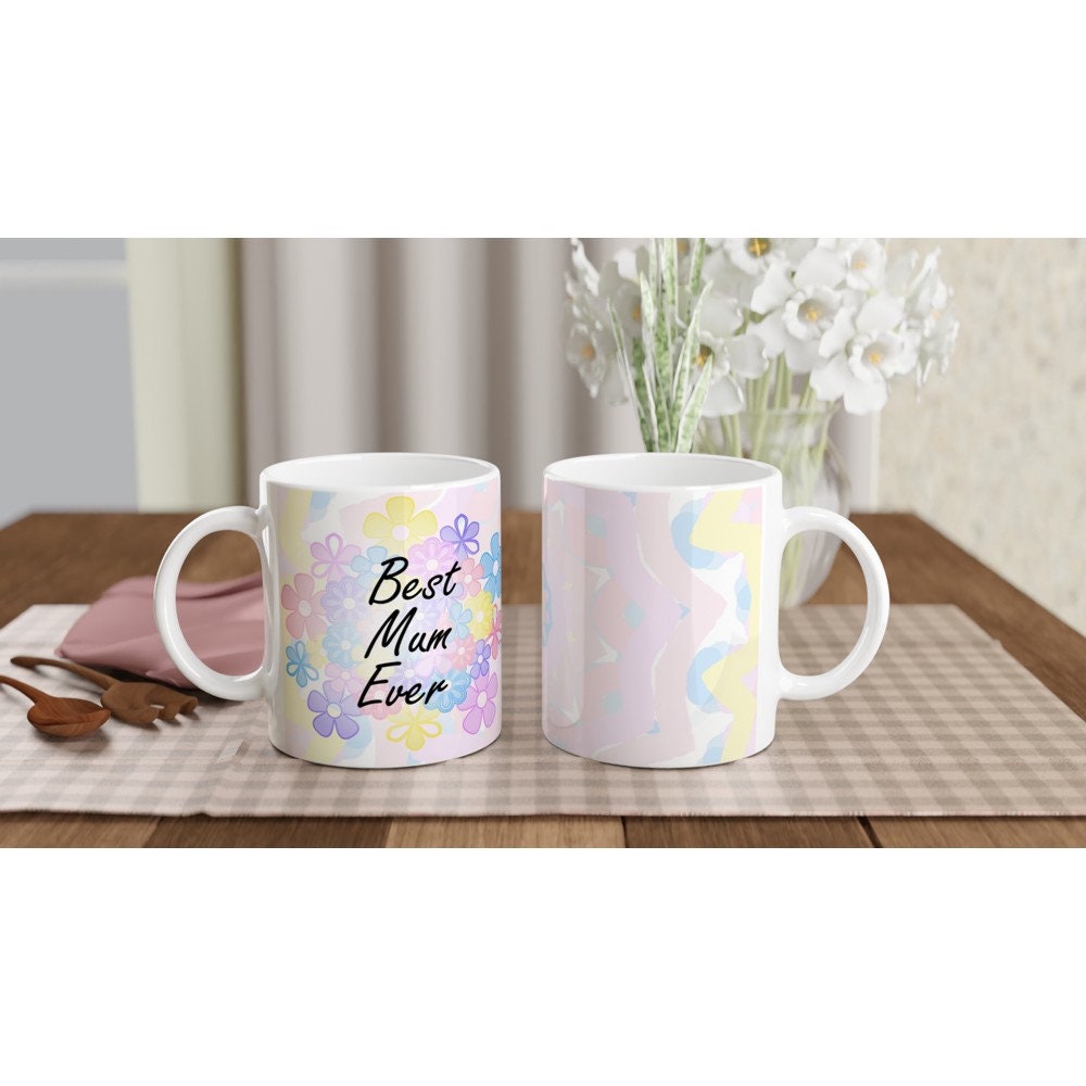 Front and back view of two white ceramic mug with the words "Best Mum Ever" written on it, with a background of pastel coloured flowers.