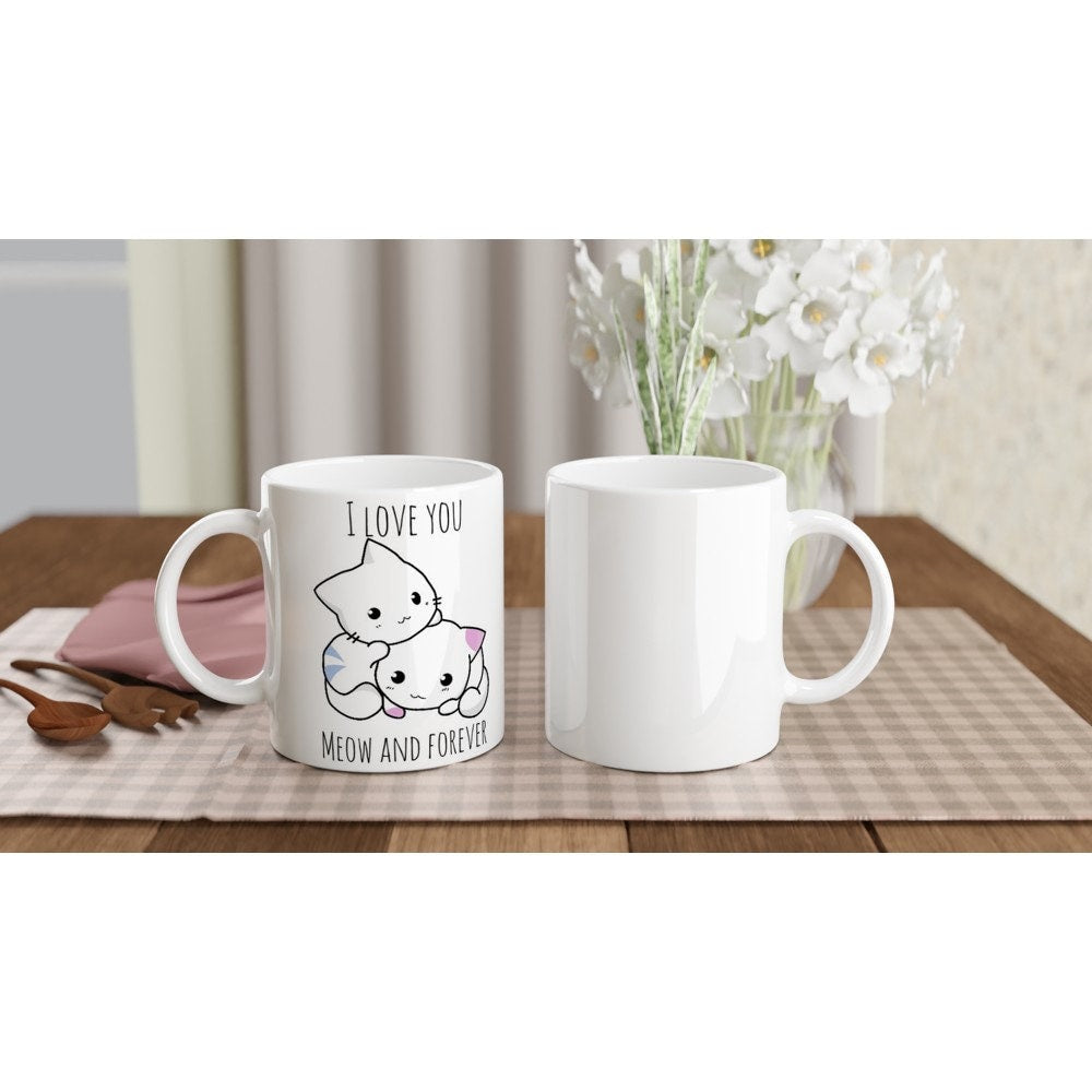 The front and back views of a white ceramic mug with the pun, "I love you meow and forever" and a picture of a blue and white striped cat next to a white and pink spotted cat.