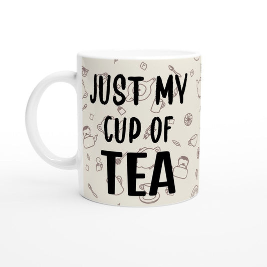 A white ceramic mug with bold black text saying, "Just my cup of tea" and line drawings of tea themed items brown on an off white background.