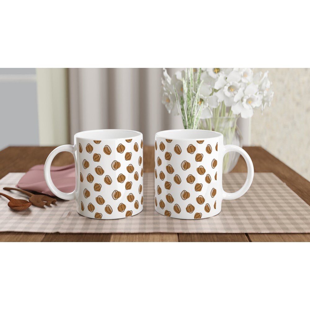 Front and back views of 2 white ceramic mug with a pattern of abstract brown coffee beans all over it, on a table.