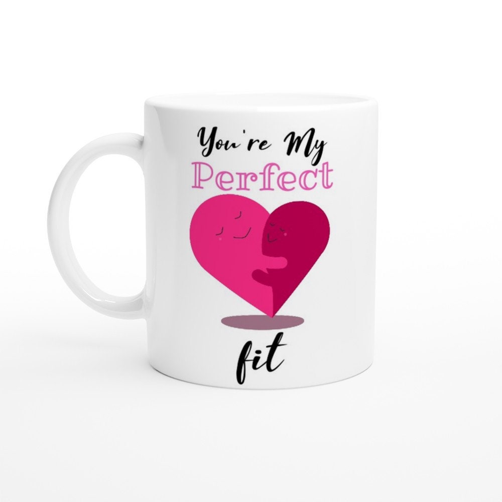 A white ceramic mug with the words, "you're my perfect fit" written on it and am image of a pink hear made of two halves which are facing each other, smiling and hugging.