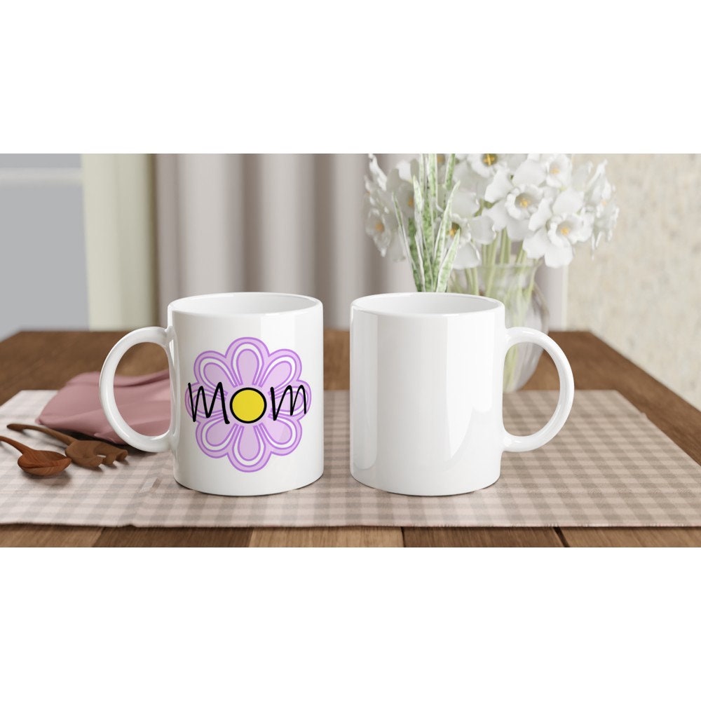 The front and back view of 2 white ceramic mugs with the words "Mom" printed on it in black and a large purple flower in the background.