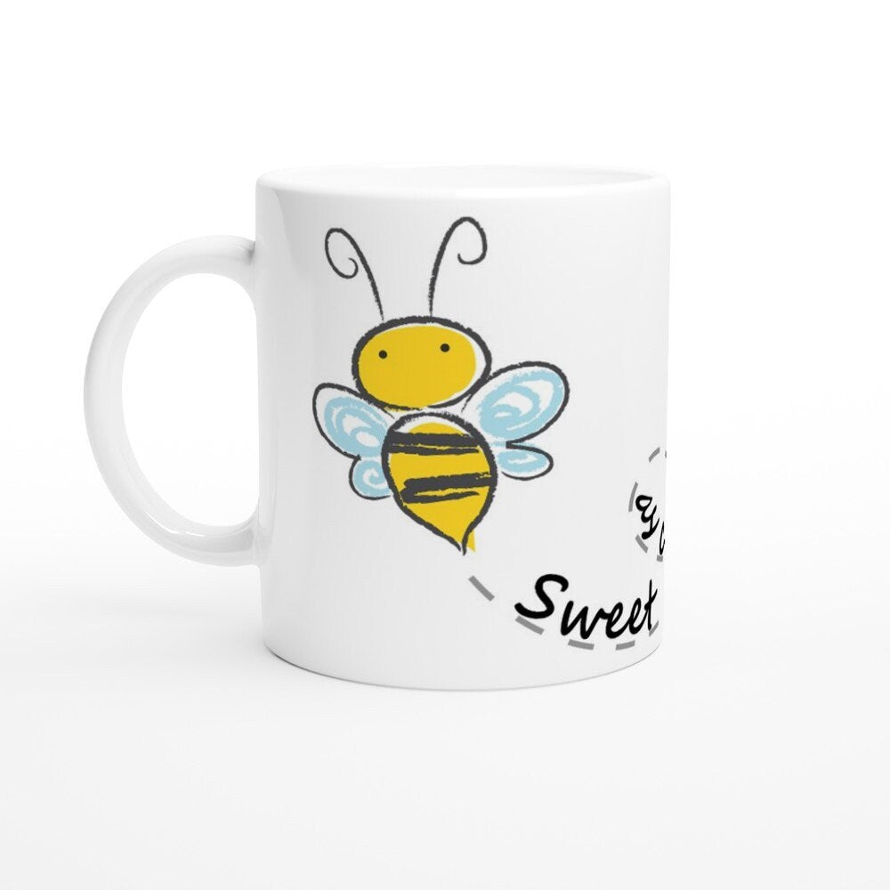 A white ceramic mug with black text saying, "Sweet as can bee" and the image of a drawing of a bee and it's path across the cup.