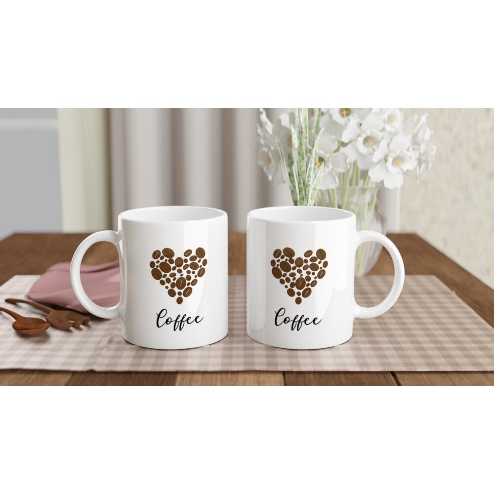 The front and back view of a white ceramic mug with the word "coffee" in black and a picture of a heart made out of coffee beans above it.