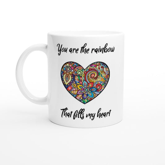 A white ceramic mug with the words "You are the rainbow that fills my heart" in black and a picture of a hear with multicoloured rainbow intricate designs.