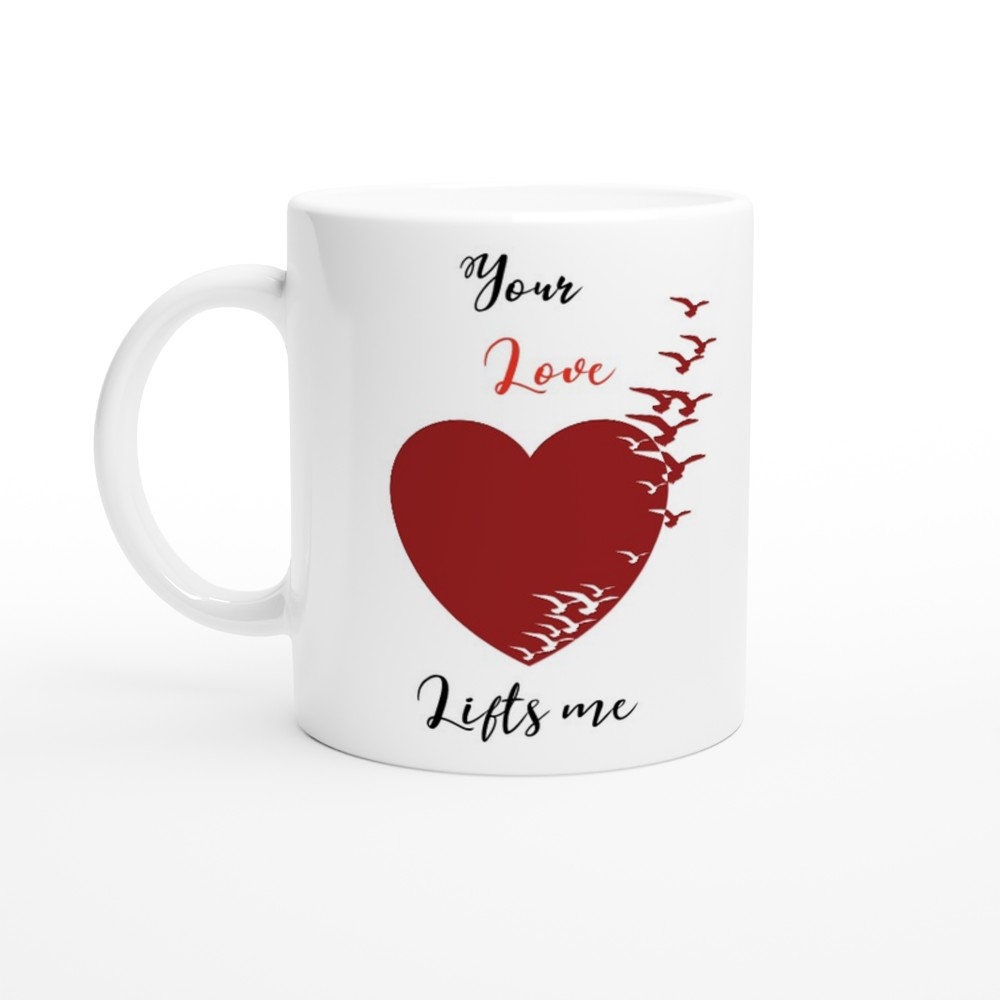 A white ceramic mug with the words, "your love lifts me" and an image of a red heart turning into birds.