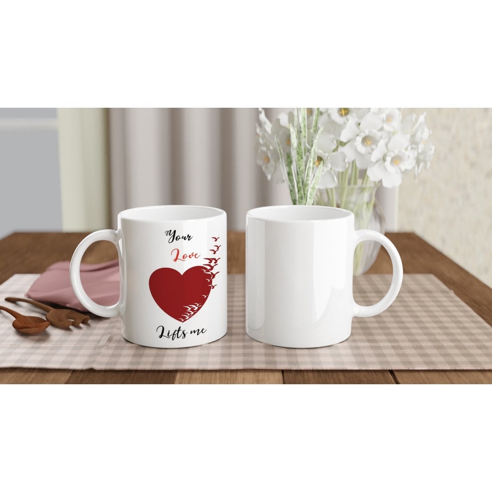 The front and back view of a white ceramic mug with the words, "your love lifts me" and an image of a red heart turning into birds.